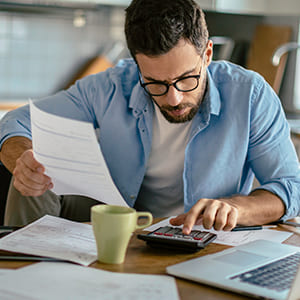 man using calculator to complete paperwork in home