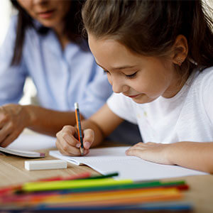 young girl working at table with mom using colored pencils and paper