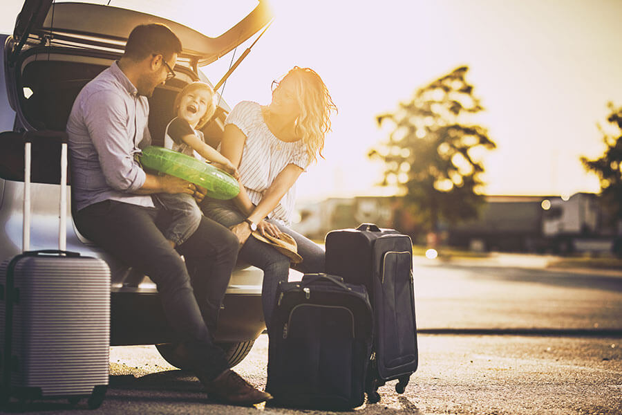 family sitting with packed bags on trunk of vehicle