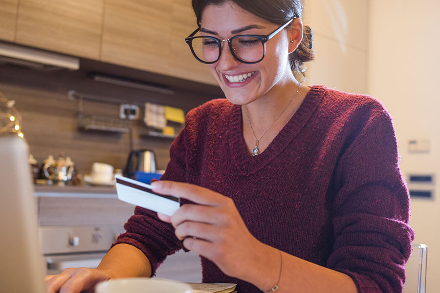 young woman sitting at table in kitchen holding a re-loadable card looking at computer