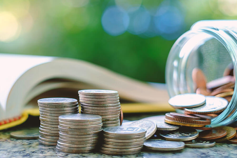 money coins stacked up on table with jar of coins and book in background